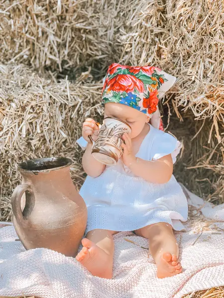 Vazonun yanında battaniyenin üzerinde oturan bir kız bebek.