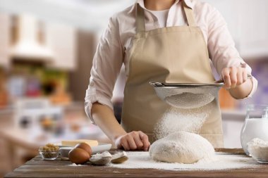 Önlük giymiş olgun bir kadın ekmek pişiriyor ya da evdeki sıcak mutfakta turta yapıyor..