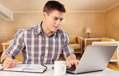 Çalışma masasında oturmuş notlar alan neşeli adam.