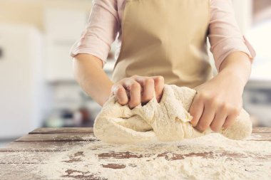 Önlük giymiş olgun bir kadın ekmek pişiriyor ya da evdeki sıcak mutfakta turta yapıyor..