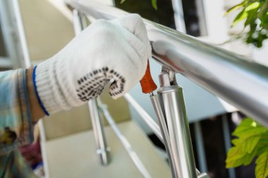 Eldivenli bir işçi, bir tornavida ve matkap kullanarak merdiven korkuluklarını tamir eder.