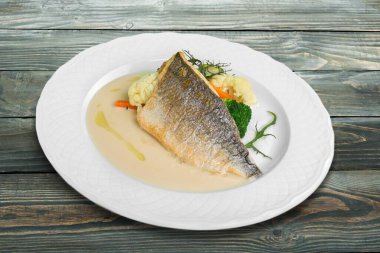 Taze pişmiş balık otlar ve sebzelerle süslenmiş ahşap bir yastıkta..