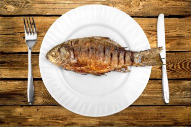 Çatal ve bıçakla beyaz tabakta kızarmış balık, yakın plan.