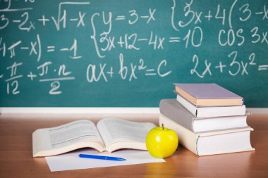 Okul kitapları, karatahtanın önündeki masada bir elma.