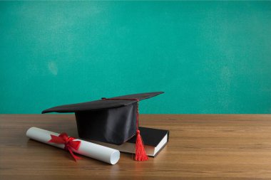 Mezuniyet şapkası, diploması ve yeşil arka plan kitabı.