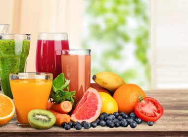 Farklı meyve suları ve taze meyvelerle dolu ahşap tepsi.