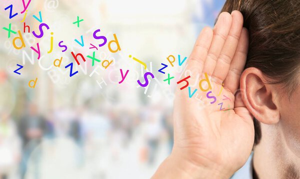 Бизнесмен держит руку у уха и что-то слушает.
