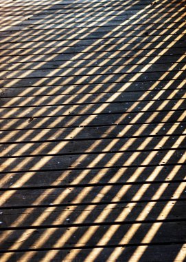 Tahta korkuluklu, tahta geçitteki gölgeler çapraz kutular oluşturuyor.