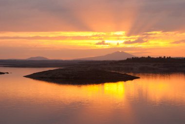 Gabriel Galan rezervuarındaki güneş ışınlarından parlayan turuncu gökyüzü Extremadura
