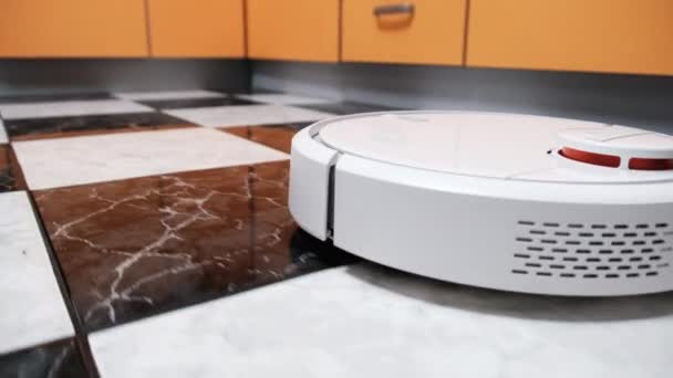 Το ρομπότ ηλεκτρική σκούπα καθαρίζει στο σύγχρονο σπίτι στο πάτωμα πλακάκια στην κουζίνα — Αρχείο Βίντεο