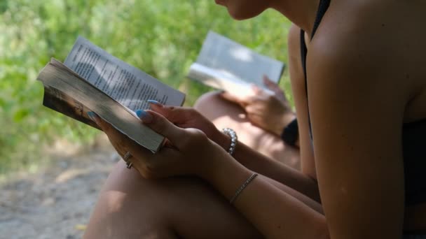 夏の日に自然の中で草の上に座って本を読む2人の若い女性 — ストック動画