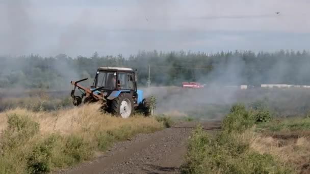 Fuoco erba secca in campo vicino al villaggio in estate, trattore spegnere il fuoco — Video Stock