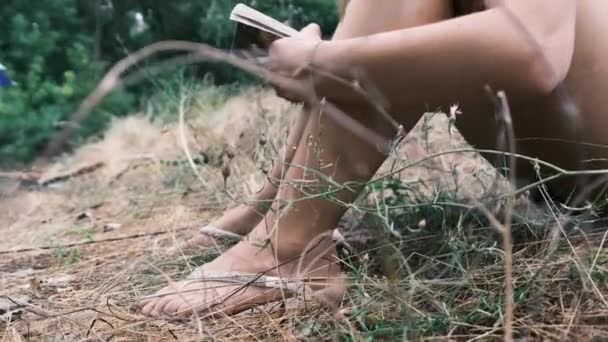 若い女性が夏の日に自然の中で草の上に座って本を読む — ストック動画