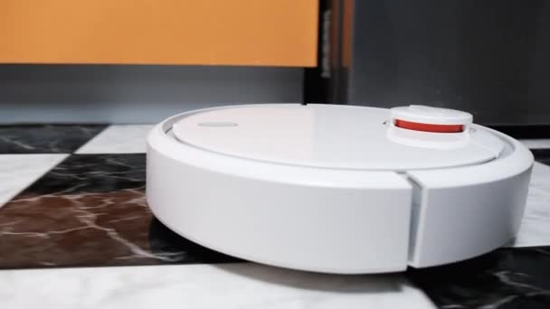 De Robot Stofzuiger reinigt in het moderne huis op de tegelvloer in de keuken — Stockvideo