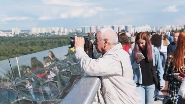 En eldre mann fotograferer byens panorama fra broen.. – stockvideo