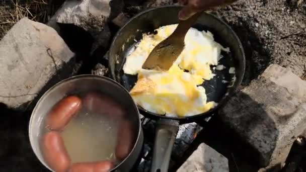 Приготовление яиц и колбас на костре в туристической сковороде в природе — стоковое видео