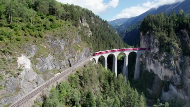Вид с воздуха на движущийся красный поезд вдоль виадука Landwasser в швейцарских Альпах — стоковое видео