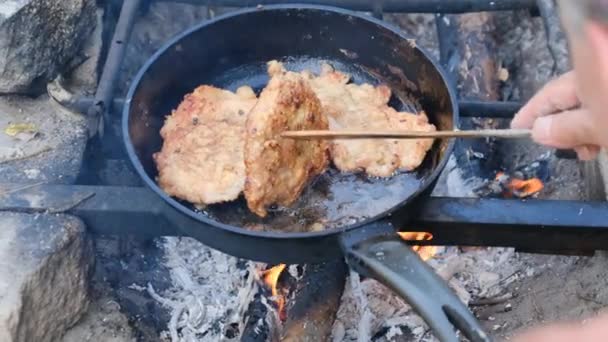 Homem cozinhando costeletas de porco fritas em óleo na frigideira sobre fogo ao ar livre, carne gorda — Vídeo de Stock