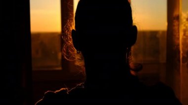 Silhouette of Young Woman Goes to the Window at Sunset, Rear View, Slow Motion