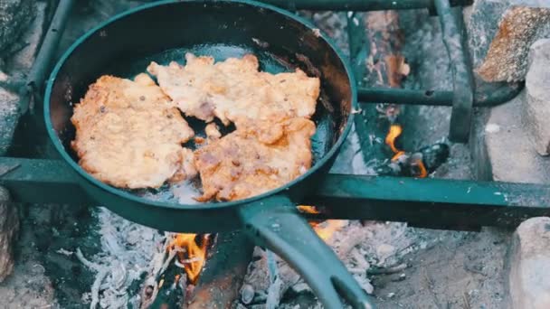 Hombre cocinando chuletas de cerdo frito en aceite en sartén sobre fuego al aire libre, carne grasa — Vídeo de stock