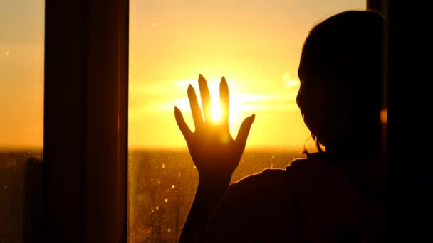 Силуэт Женщина у окна, кладущая руку к стеклу сквозь лучи заката Медленное движение — стоковое видео