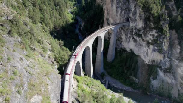 Légi felvétel egy mozgó piros vonat mentén Landwasser Viaduct a svájci Alpokban — Stock videók