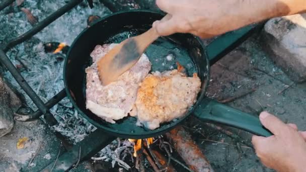 Muž vaření smažené vepřové kotlety v oleji v pánvi nad ohněm venkovní, mastné maso — Stock video