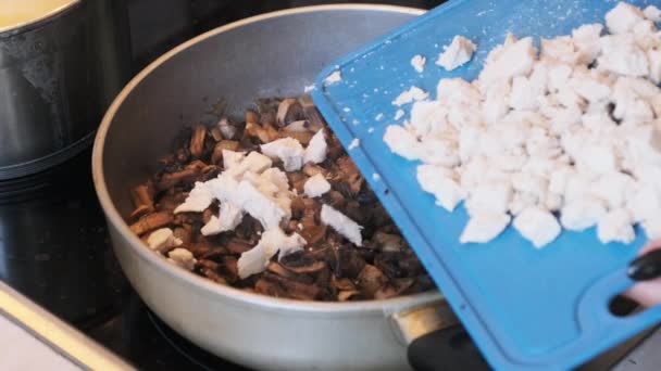 Händerna på en ung kvinna som lägger hackat kött till stekta svampar i en varm kastrull — Stockvideo
