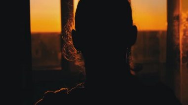 Silhouette of Young Woman Goes to the Window at Sunset, Rear View, Slow Motion
