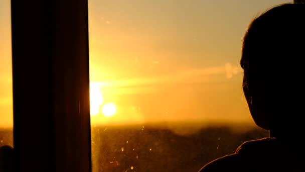 Силуэт молодой женщины, смотрящей в окно на закате, медленное движение — стоковое видео