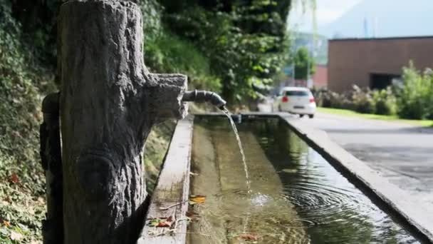 Hegyi víz ömlik a csapból egy fa konténerbe a Liechtenstein Streeten — Stock videók