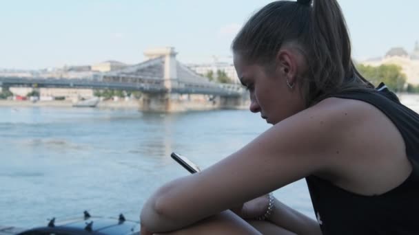 Jeune femme utilise Smartphone en plein air sur le quai dans le parc près de la rivière — Video