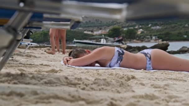 Niski kąt widzenia młodej dziewczyny leżącej i opalającej się na piaszczystej plaży — Wideo stockowe