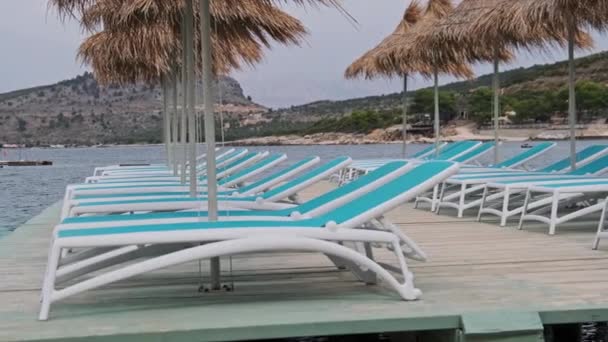 Άδειο Sun Loungers με Straw ομπρέλες στη σειρά στην προβλήτα από την παραλία στο Turquoise Sea — Αρχείο Βίντεο