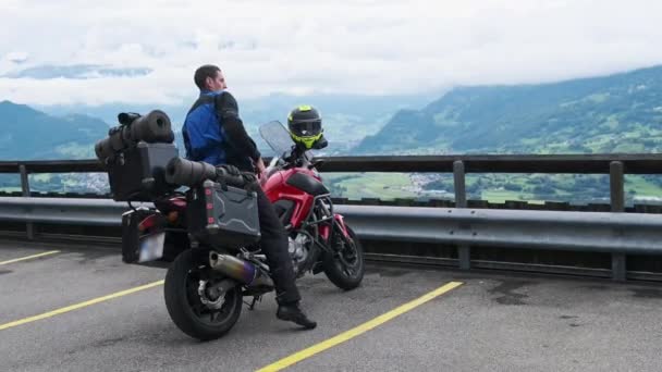 Байкер на туристическом мотоцикле с багажными сумками стоит на горном ландшафте, Альпы — стоковое видео