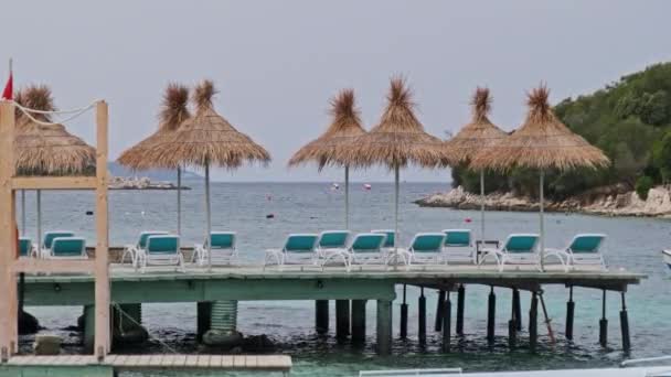 Reposeras vacías con sombrillas de paja en fila en Pier by Beach en el mar Turquesa — Vídeo de stock