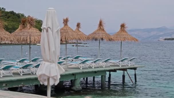 Empty Sun Loungers with Straw Umbrellas in Row on Pier by Beach in Turquoise Sea — Stok Video