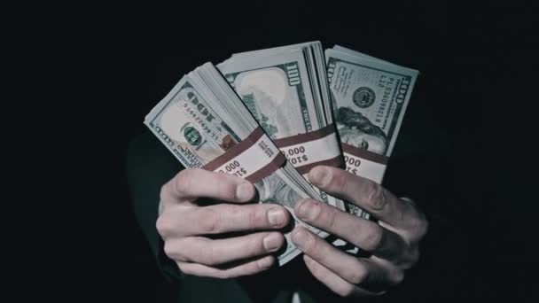 Три пачки по 10000 американских долларов бандлы в мужских руках на черном фоне — стоковое видео