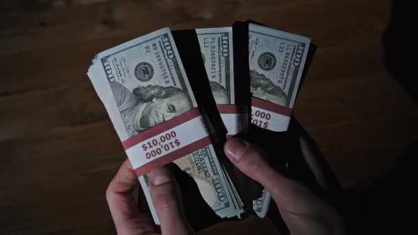 Mãos masculinas seguram três pilhas de 10000 dólares americanos contas em fundo de madeira — Vídeo de Stock