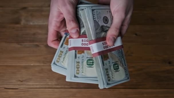 Мужские руки переворачивая стеки 10000 долларов счета на деревянном фоне, медленное движение — стоковое видео