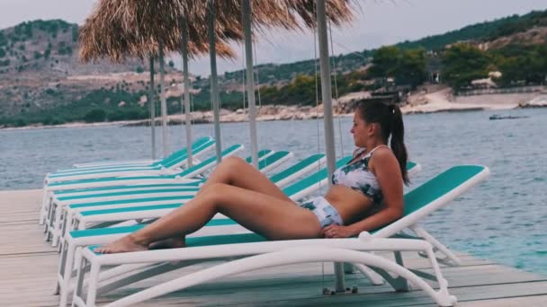 Attraktiv kvinna Sola på däck stol under halmparaply av turkost hav — Stockvideo