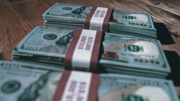 Tres pilas de billetes de 10000 dólares americanos en paquetes yacen sobre una mesa de madera — Vídeo de stock