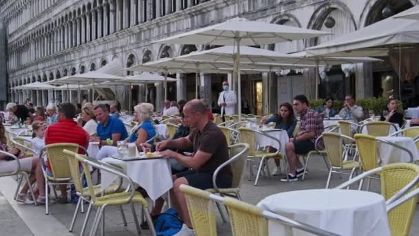Touristen sitzen an den Tischen der Restaurants und Cafés auf dem Markusplatz — Stockvideo