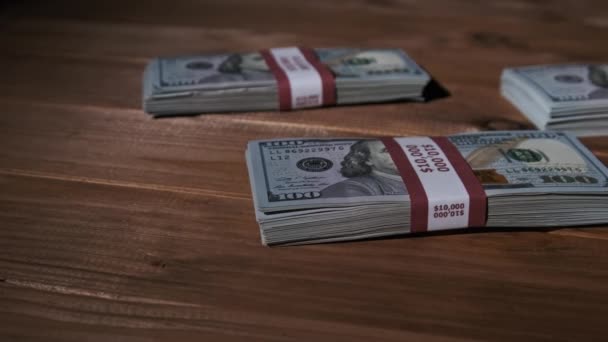 Tres pilas de billetes de 10000 dólares americanos en paquetes yacen sobre una mesa de madera — Vídeos de Stock