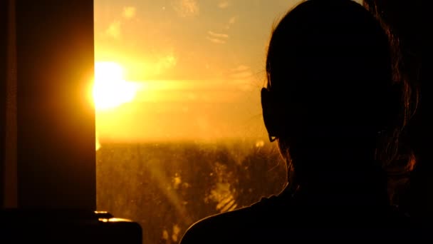 Silhouet van een jonge vrouw op zoek uit het raam bij zonsondergang, Slow Motion — Stockvideo