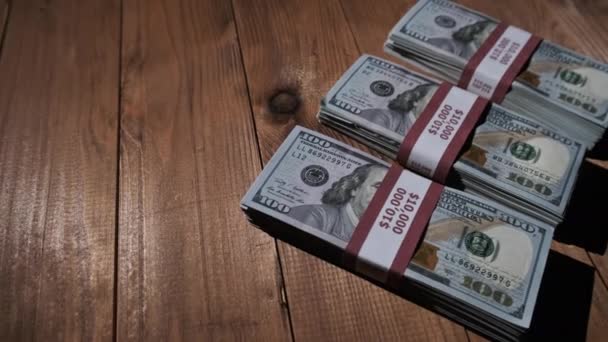 Tres pilas de billetes de 10000 dólares americanos en paquetes yacen sobre una mesa de madera — Vídeos de Stock