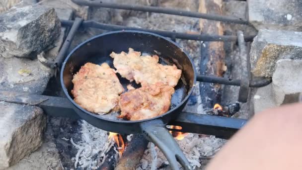 Hombre cocinando chuletas de cerdo frito en aceite en sartén sobre fuego al aire libre, carne grasa — Vídeo de stock