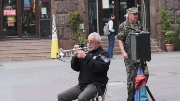 Вуличний музикант грає на трубі, сидячи на стільці на вулиці — стокове відео