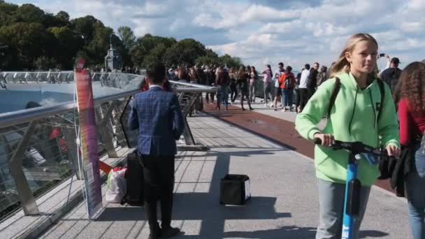Giovane musicista di strada suona il sassofono nel parco pubblico, la gente cammina passato — Video Stock