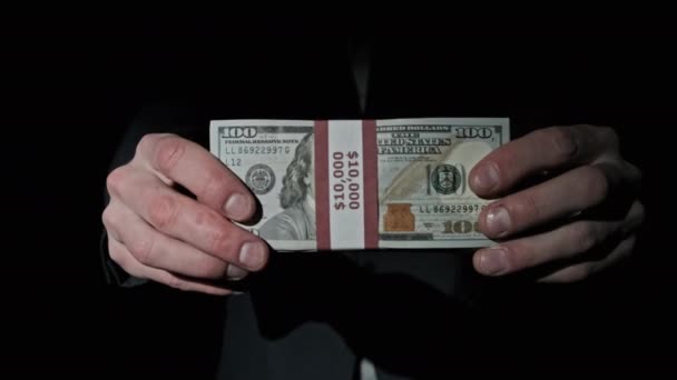 Бізнесмен в костюмі показує стек 10000 американських доларів на чорному тлі — стокове відео